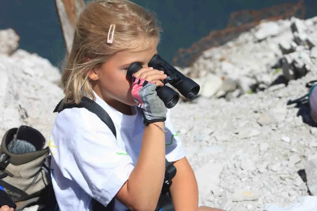 Kind beobachtet die Natur und Felsenblöcke der Dolomiten mit einem Fernglas